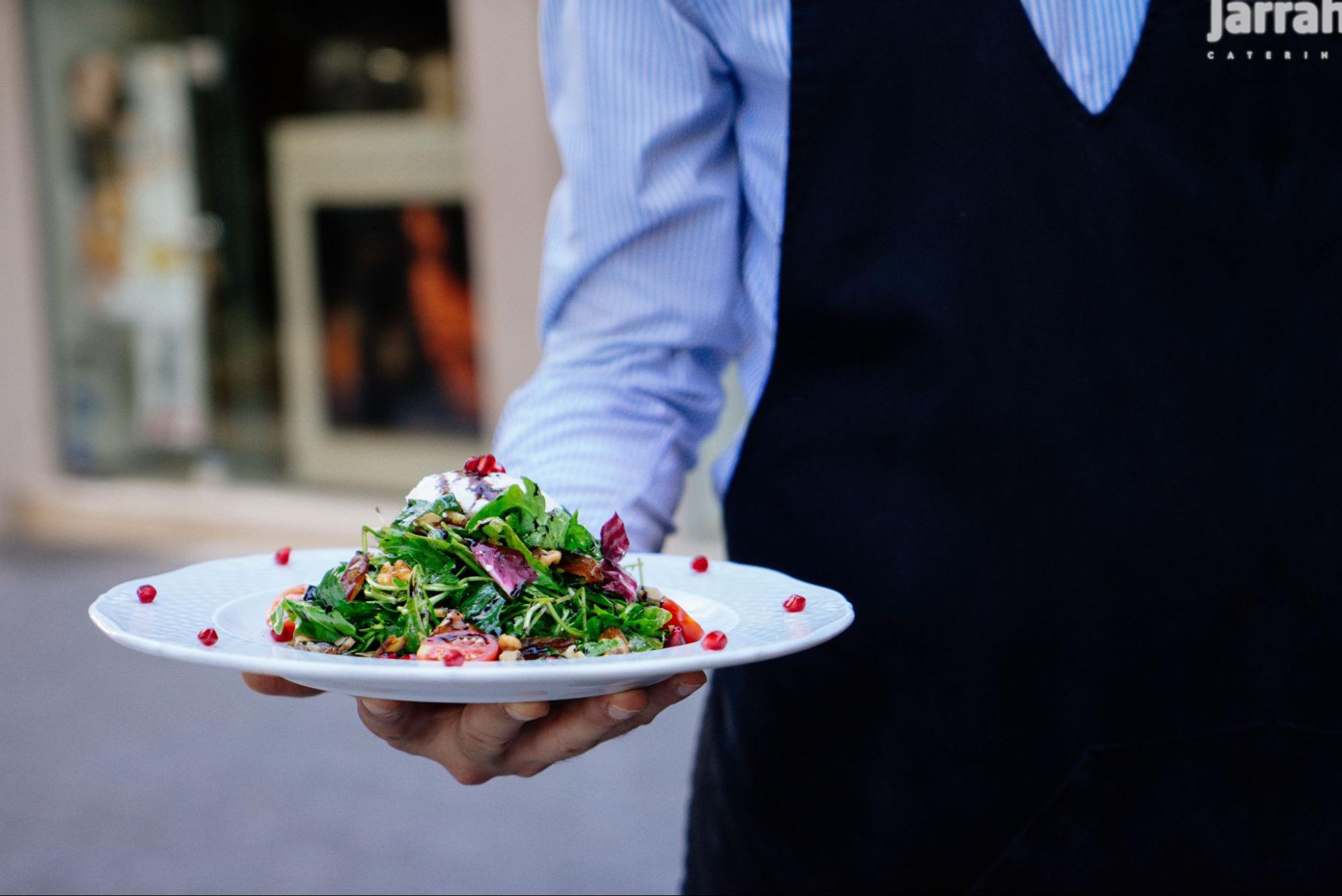 Jarrah Catering staff member presenting a fresh salad at a catered event.